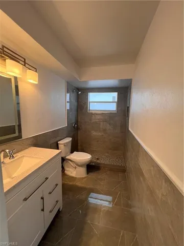 Bathroom featuring a tile shower, tile walls, vanity, and toilet