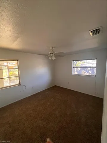 Unfurnished room with dark colored carpet and ceiling fan