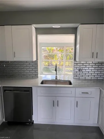 Kitchen featuring dishwasher, sink, decorative backsplash, and white cabinets