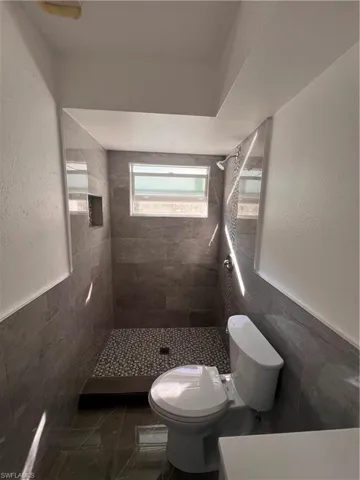 Bathroom featuring tiled shower, toilet, and tile walls