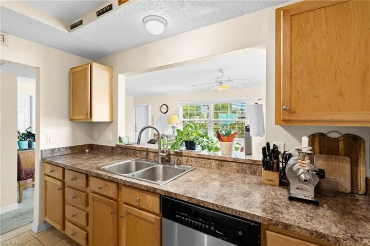 Kitchen featuring dishwasher, a ceiling fan, a textured ceiling, dark countertops, and light wood finish cabinets
