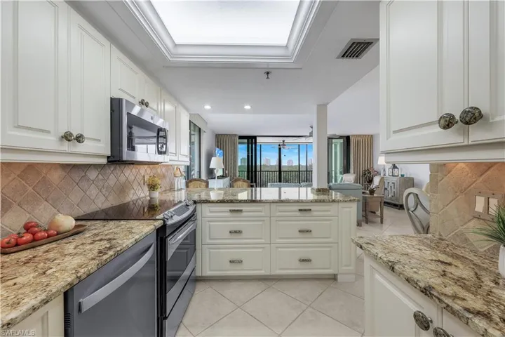 Kitchen featuring white cabinetry, granite countertops, stainless steel appliances, a tiled backsplash, and an island with drawer storage