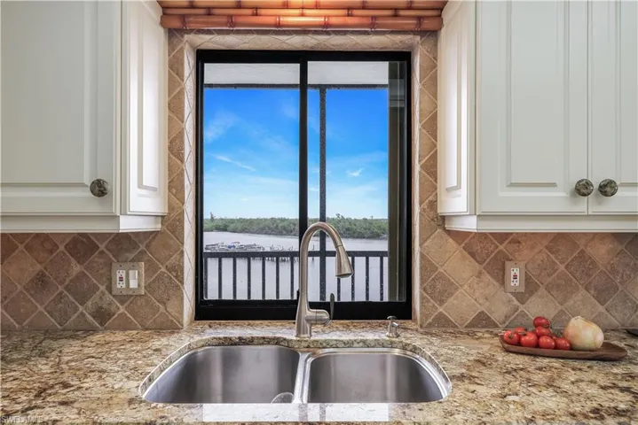 Double stainless steel sink, pull-down faucet, granite-style countertop, tiled backsplash, and white cabinetry