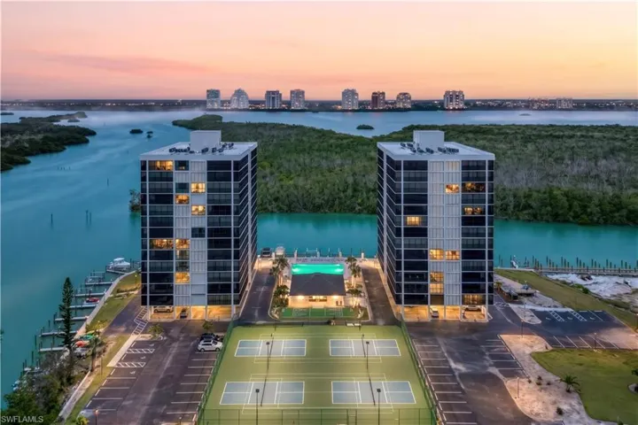 Two high-rise buildings with balconies, tennis courts, a swimming pool, and a marina with docked boats
