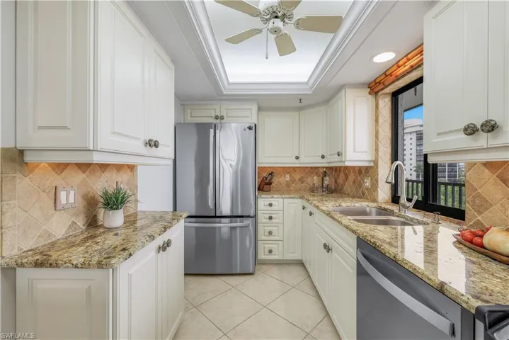 White cabinetry with decorative pulls, granite countertops, stainless steel appliances, tile flooring, and tile backsplash