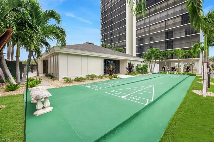 Shuffleboard court with manicured lawn, palm trees, and a low-rise building