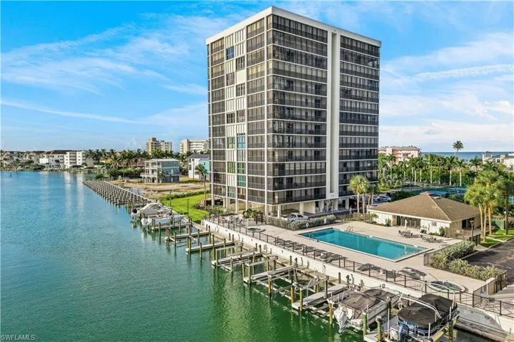 High-rise condominium building featuring multiple private balconies, a waterfront swimming pool, and a spa