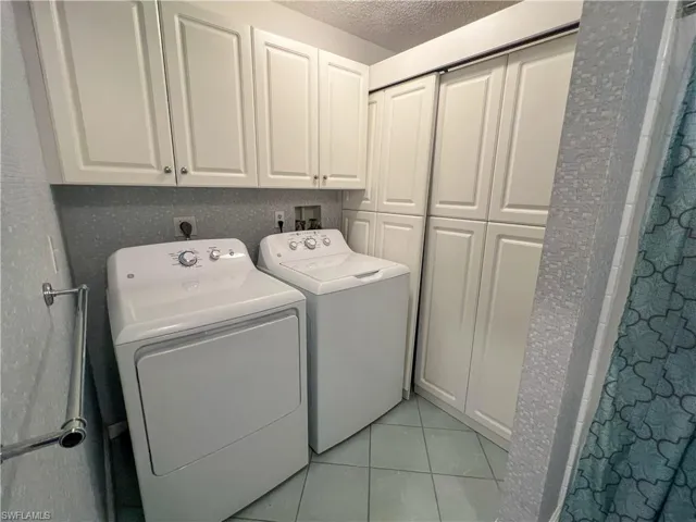 Washroom featuring light tile patterned flooring, a textured ceiling, washing machine and clothes dryer, and cabinet space