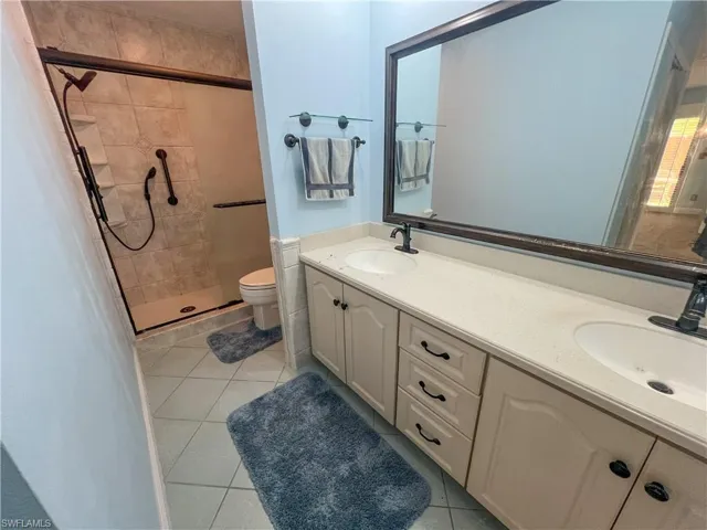 Full bath featuring double vanity, a shower stall, and light tile patterned flooring