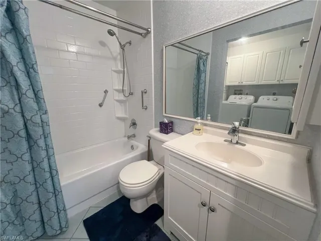 Full bath with shower / bath combo with shower curtain, washer and clothes dryer, vanity, and light tile patterned flooring