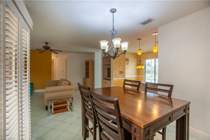 Dining room with wallpapered walls, a textured ceiling, a chandelier, light tile patterned flooring, and a ceiling fan