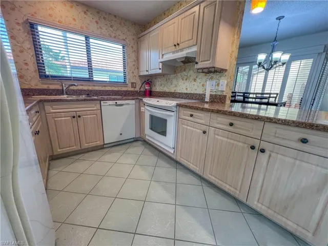 Kitchen featuring wallpapered walls, hanging light fixtures, a chandelier, white appliances, and under cabinet range hood