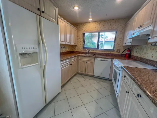 Kitchen with white appliances, wallpapered walls, a textured ceiling, light tile patterned floors, and under cabinet range hood