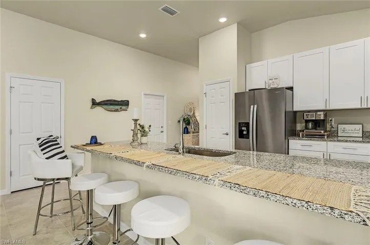 Kitchen with stainless steel fridge, white cabinetry, a kitchen breakfast bar, light stone countertops, and a high ceiling