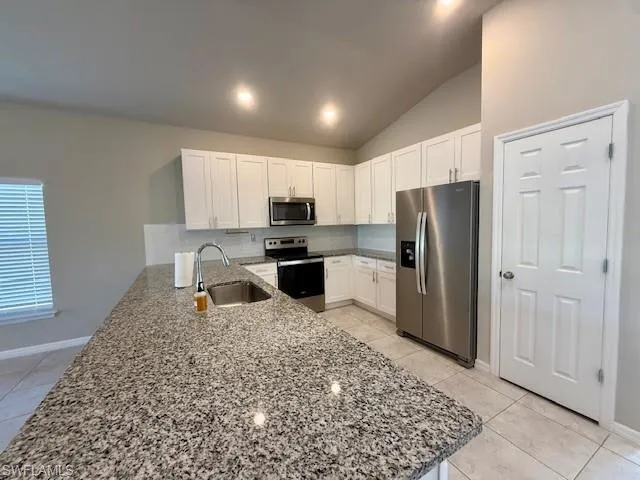 Kitchen with light stone countertops, stainless steel appliances, a peninsula, white cabinets, and lofted ceiling