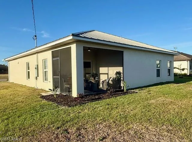 Rear view of property featuring stucco siding, a lawn, a sunroom, and a metal roof