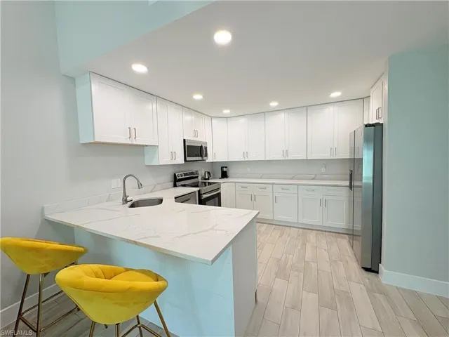 Kitchen with a peninsula, light stone counters, stainless steel appliances, white cabinets, and a kitchen breakfast bar