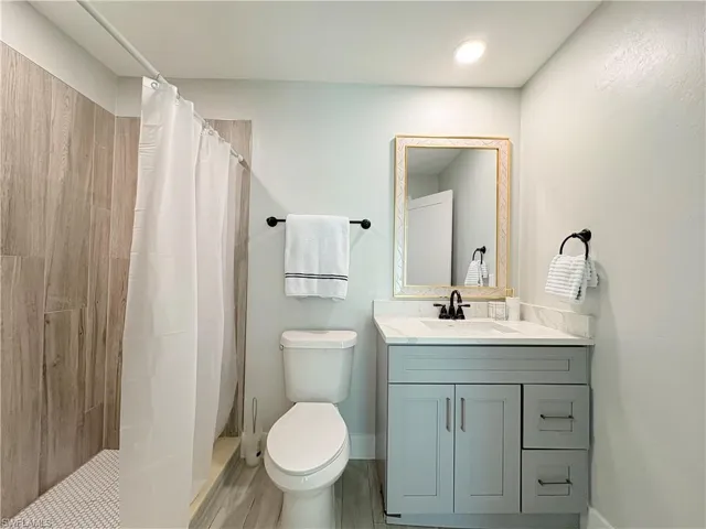 Full bath featuring a tile shower, vanity, and wood finish floors