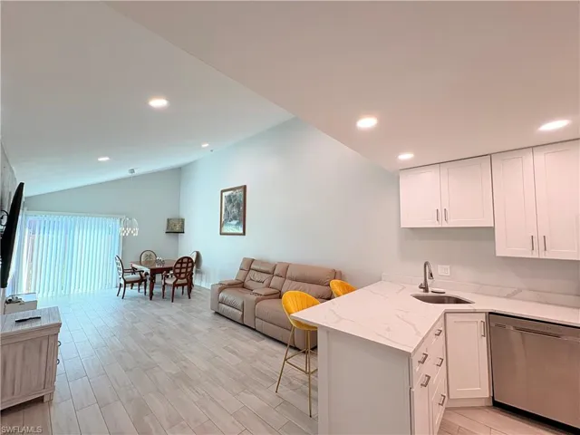 Kitchen with dishwasher, a peninsula, lofted ceiling, light stone countertops, and white cabinets