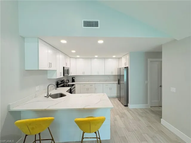 Kitchen with light stone counters, appliances with stainless steel finishes, recessed lighting, white cabinets, and a breakfast bar