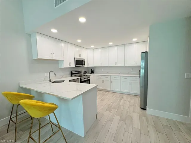 Kitchen with a peninsula, stainless steel appliances, white cabinets, light stone countertops, and a breakfast bar area