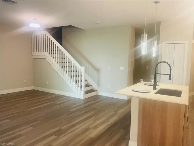 Kitchen with hanging light fixtures, dark wood finished floors, light stone countertops, open floor plan, and brown cabinetry