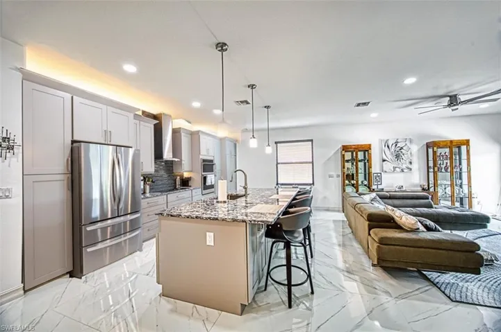 Kitchen with appliances with stainless steel finishes, an island with sink, wall chimney exhaust hood, ceiling fan, and a kitchen bar
