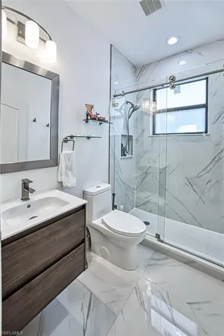 Bathroom featuring tile flooring, vanity, toilet, and a shower with door