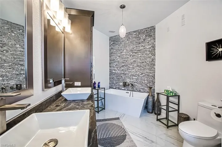 Bathroom with a bath, tile flooring, toilet, and dual bowl vanity