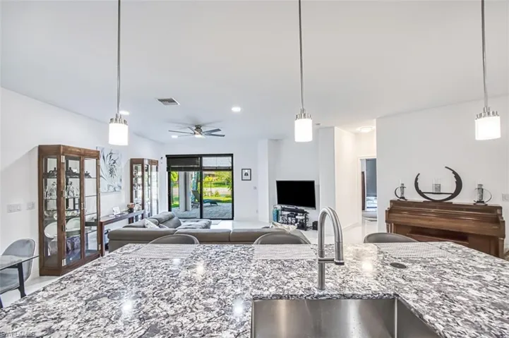 Kitchen with hanging light fixtures, ceiling fan, light stone counters, and sink