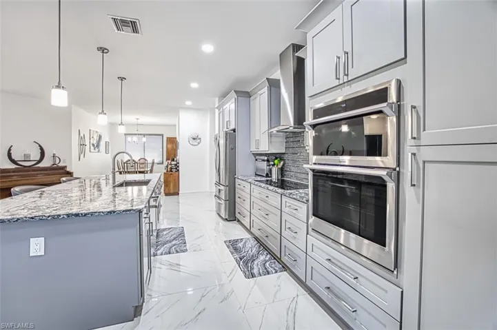 Kitchen with tasteful backsplash, stainless steel appliances, a center island with sink, decorative light fixtures, and wall chimney exhaust hood