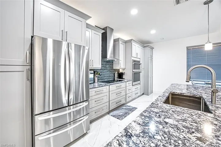 Kitchen featuring hanging light fixtures, stainless steel appliances, wall chimney exhaust hood, sink, and tasteful backsplash