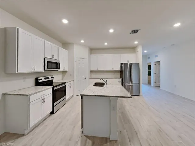 photo is of a previously completed home  Kitchen featuring white cabinetry, sink, appliances with stainless steel finishes, and an island with sink