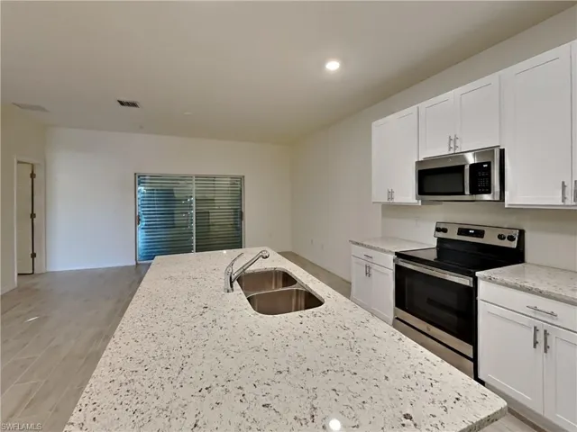 photo is of a previously completed home  Kitchen with sink, white cabinetry, stainless steel appliances, and a kitchen island with sink