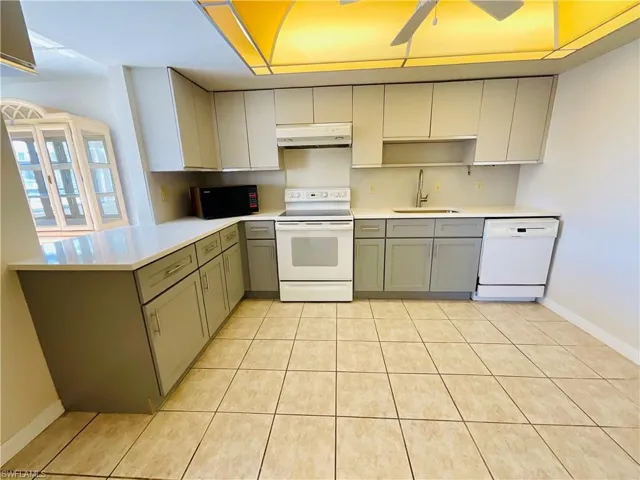 Kitchen featuring kitchen peninsula, sink, light tile patterned floors, and white appliances