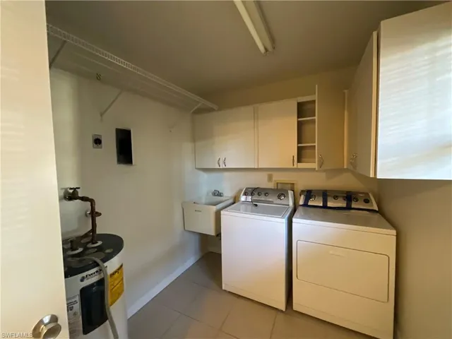 Clothes washing area featuring cabinets, sink, water heater, light tile patterned floors, and washing machine and dryer