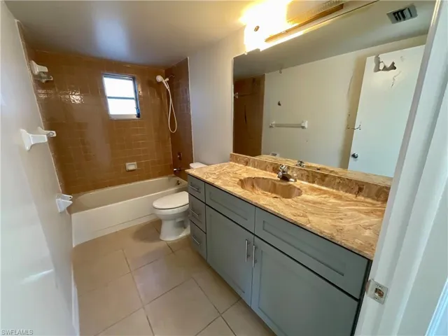 Full bathroom with toilet, vanity, tile patterned floors, and tiled shower / bath combo