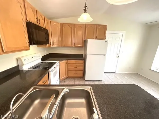 Kitchen featuring white appliances, lofted ceiling, pendant lighting, light tile patterned floors, and light brown cabinets