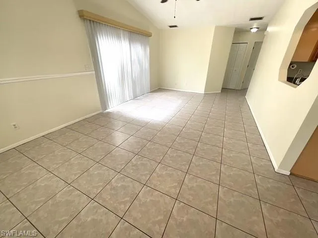 Empty room with light tile patterned floors, ceiling fan, and vaulted ceiling