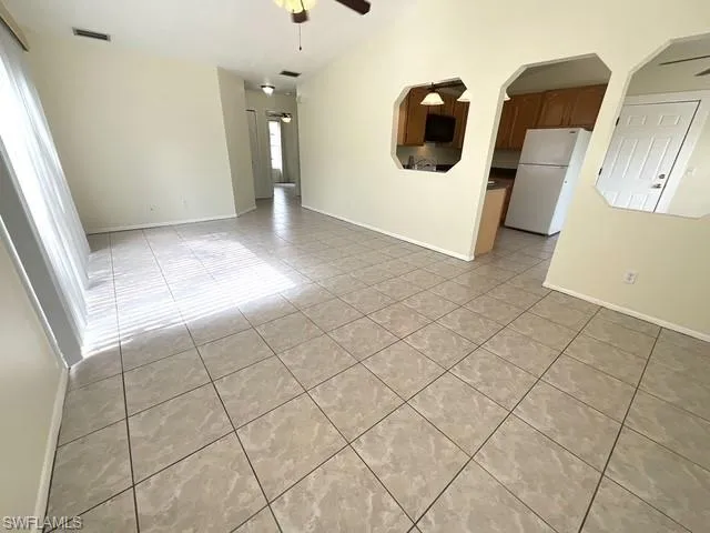 Empty room featuring ceiling fan, light tile patterned floors, and arched walkways