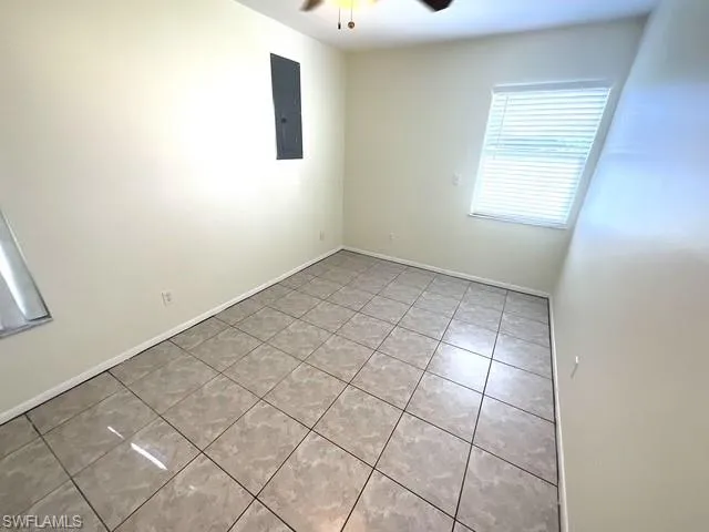 Empty room with light tile patterned floors, ceiling fan, and electric panel