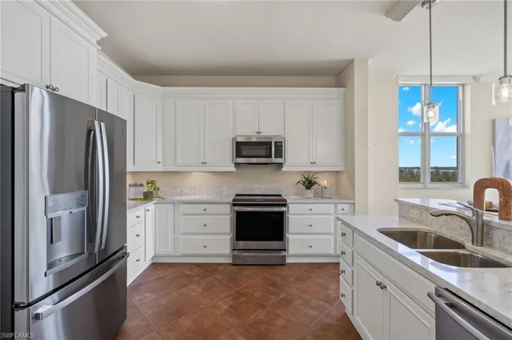 Kitchen featuring dark tile patterned floors, white cabinets, stainless steel appliances, light stone countertops, and sink
