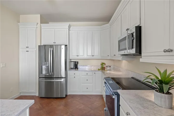 Kitchen with white cabinets, dark tile patterned floors, and appliances with stainless steel finishes