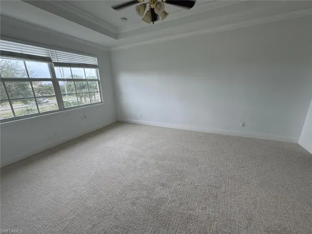 Carpeted empty room featuring a raised ceiling, ceiling fan, and crown molding