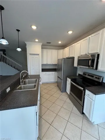 Kitchen with light tile patterned flooring, white cabinetry, sink, appliances with stainless steel finishes, and decorative light fixtures