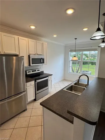 Kitchen featuring sink, appliances with stainless steel finishes, decorative light fixtures, an island with sink, and white cabinets
