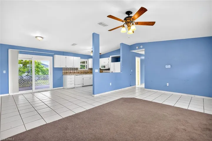 Unfurnished living room with light tile patterned floors, lofted ceiling, ceiling fan, and light colored carpet