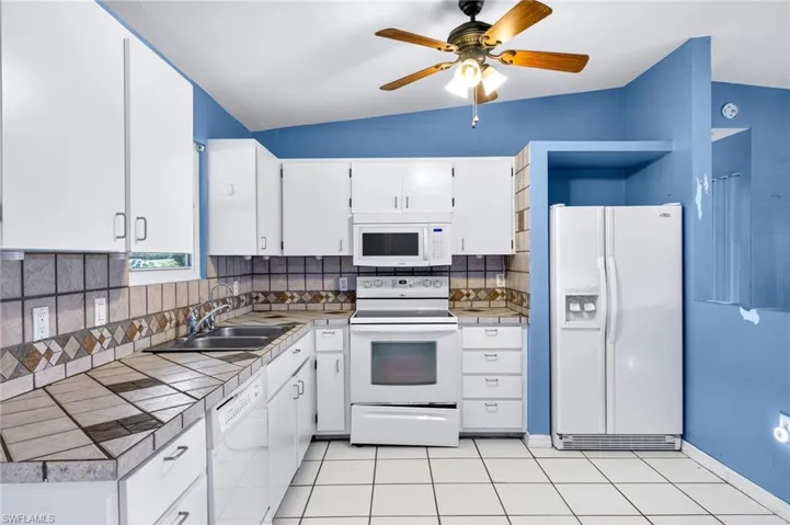 Kitchen with tile counters, white appliances, white cabinetry, decorative backsplash, and light tile patterned floors
