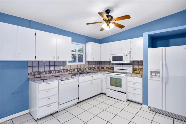 Kitchen featuring white appliances, tile countertops, white cabinets, backsplash, and light tile patterned flooring