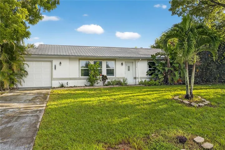 Ranch-style house featuring a garage, a front lawn, driveway, stucco siding, and a metal roof